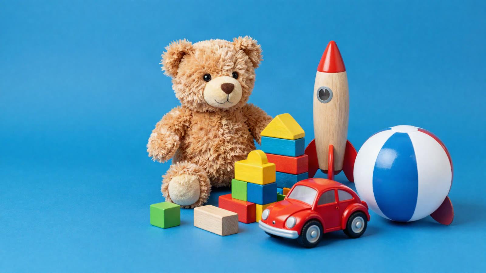 Peluche, bloques de madera, cohete, auto rojo y pelota de playa sobre fondo azul