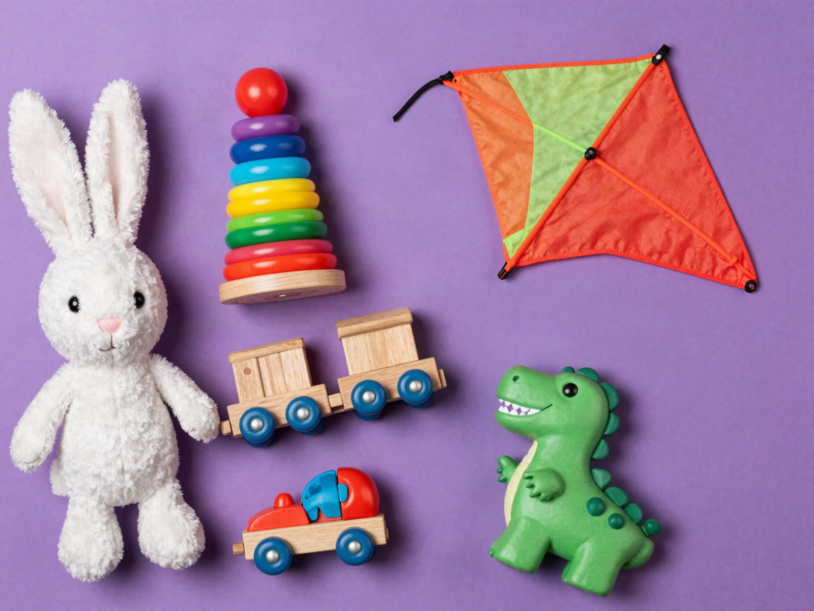 Peluche de conejo, aros apilables, tren de madera, volantín, dinosaurio y yoyó sobre fondo morado